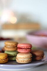 Plate of pastel macarons, cookies and chocolate, cup of tea of coffee, glass of bubble water, various berries, books and accessories on the table. Selective focus, pastel colors.