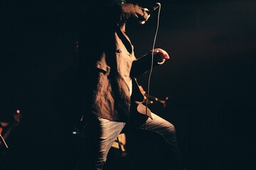 Caucasian male singer performing on the stage against a dark background - obrazy, fototapety, plakaty