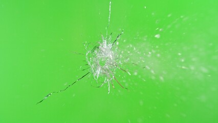 Close-up of gunshot through the glass, shattering against the green background