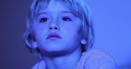 Close-up of child in front of TV screen at night, blue light