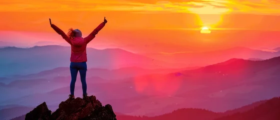 Poster A woman, in celebration of reaching the summit of a mountain peak at sunset or sunrise, holds her arms high above her head in elation. © Zaleman
