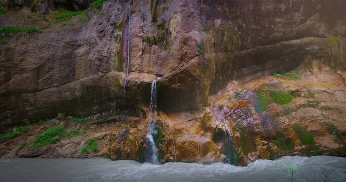 Chegem waterfalls. An amazing stream of water flows like a waterfall from a stone wall directly into a stormy river. Russia. Caucasus. Kabardino-Balkarian Republic.