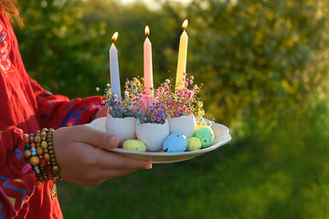 plate with candles and flowers in eggs shells in hands girl outdoor, natural background. symbol of...