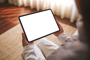 Mockup image of a woman holding digital tablet with blank desktop screen while sitting on a sofa at...