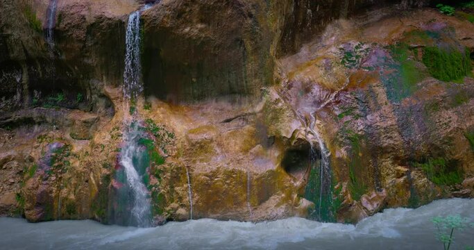 Chegem waterfalls. An amazing stream of water flows like a waterfall from a stone wall directly into a stormy river. Russia. Caucasus. Kabardino-Balkarian Republic.