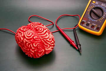 Representation of a human brain in red next to a machine for measuring electrical impulses on a dark background.
