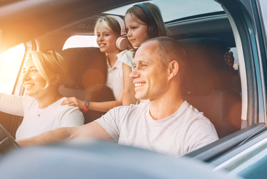 Happy smiling young couple with two daughters inside car during auto trop. They are smiling, and laughing during a road trip. Family values, tatraveling, automotive industry concept.