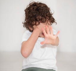 A young boy with curly black hair covering his face with his hands