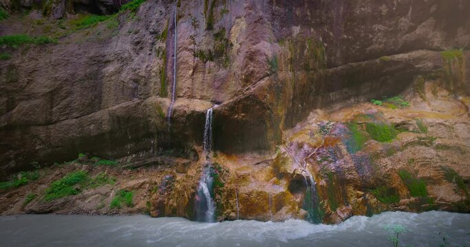 Chegem waterfalls. An amazing stream of water flows like a waterfall from a stone wall directly into a stormy river. Russia. Caucasus. Kabardino-Balkarian Republic.