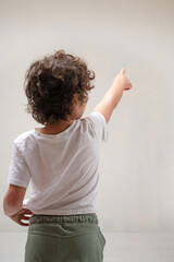 Young boy pointing with happy gesture at a white wall