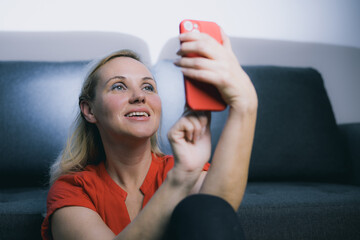 Young lady, woman in a red dress with a matching smart phone is taking a selfie. Mature online...