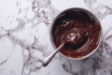 Fototapeta premium Melted dark organic chocolate in a bowl and spoon on a marble surface