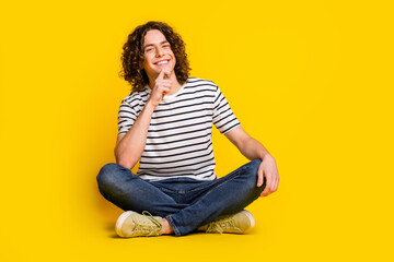 Full size portrait of nice young man sit floor think wear striped t-shirt isolated on yellow color...