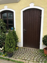 Haustüre aus Holz und Gehweg mit Kopfsteinpflaster mit Pflanzen und Blumendekoration in einer alten Fassade mit Fenster 