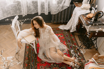 Young fashionable model wearing vintage bridal dress sitting on floor, posing at home, in stylish vintage interior - 776058125