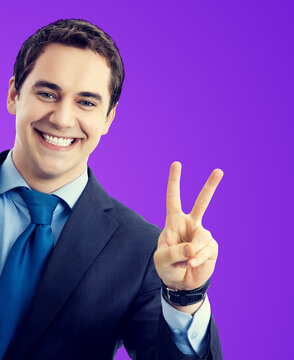 Portrait of confident businessman showing two fingers v-sign victory hand gesture, isolated against purple wall background. Middle aged happy excited smiling business man at studio concept image.
