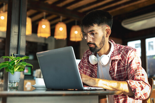 Young Asian business man with beard and glasses working on laptop computer while sitting in cafe.