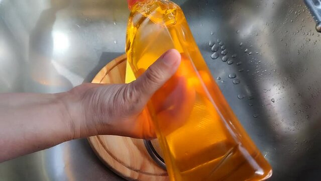 Unas manos de mujer lavando un colador de metal con una esponja amarilla con jab&oacute;n l&iacute;quido  y  agua colocada en una tabla de madera en un fregadero