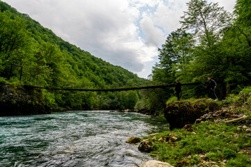 Pedestrian Bridge over the Piva River before the dam from Piva Lake was released, creating crystal clear blue watercolor, surrounded by green trees on mountains