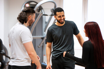 A cheerful group of two men and a woman having a conversation in a gym setting. 