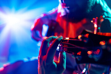 Close-up of musician's fingers on bass guitar fretboard playing melodic chords against vibrant light show. Concept of rock and classic music, hobby and work, energy, music festivals, concerts. Ad