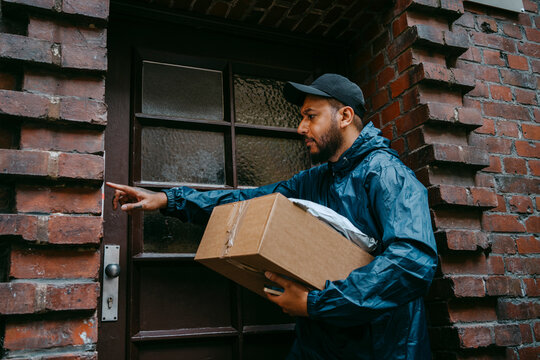 Male courier delivery person ringing doorbell while arriving with package outside house