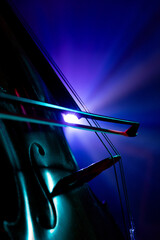 Close-up photo of cello strings and bow with soft focus on blue-purple stage lighting. Classical music instrument. Concept of hobby and work, music festivals, concerts, symphony show, culture.