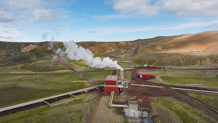 Fototapeta premium Geothermal power station in Icelandic landscape, steaming chimneys in the valley on a bright sunny day, aerial view. Energy, industry and sustainability concept.