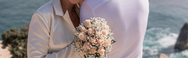 A bride and groom are hugging and the bride is holding a bouquet. Scene is happy and romantic.