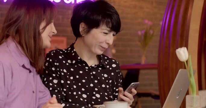 Happy women sitting together with laptops, engaged in conversation and laughter. Technology facilitates social interaction and shared moments of enjoyment in digital age. Friendship and communication.