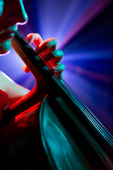 Close up, cropped portrait of musician seated, deeply focused on her cello performance under spotlights on stage. Concept of hobby and work, music festivals, concerts, symphony show, culture.