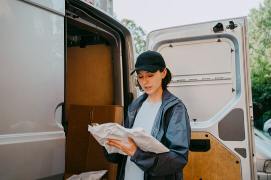 Female delivery person sorting parcel while standing near van trunk