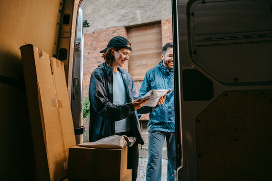 Male and female delivery coworkers sorting out parcels while standing near van