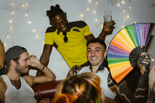 Portrait of smiling non-binary person holding multi colored hand fan while having fun with friends at nightclub