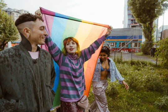 Woman holding LGBT flag while walking with non-binary friends at park