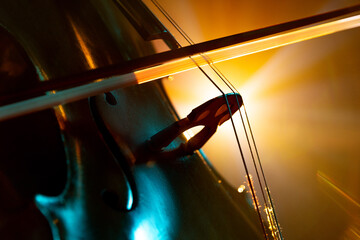 Detailed photo of classical cello with bow in golden-yellow stage light casting vibrant shadows....