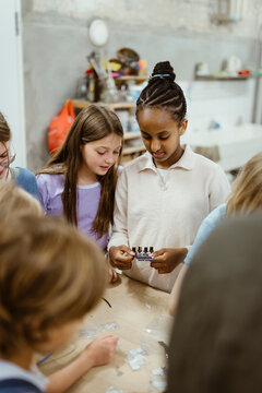 Female students holding electrical part while standing with friends in workshop