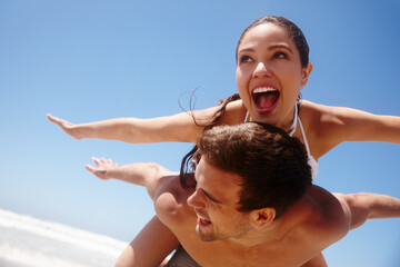 Couple, piggyback and freedom on beach with playing for bonding, summer vacation or travel...