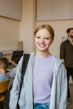 Portrait of smiling female student carrying backpack while standing in classroom at school