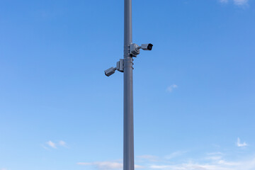 Two street surveillance cameras on pole against a blue sky background .Cameras are facing in opposite directions, full view. Security, surveillance, control concept