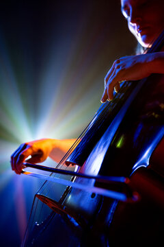 Close up portrait of talented young woman, musician, cellist performing symphony in purple-blue spotlights on stage with smoke. Concept of hobby and work, music festivals, concerts, symphony, culture.
