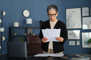 In a professional office environment, a mature Caucasian businesswoman diligently attends to documents, showcasing confidence and expertise in her field.