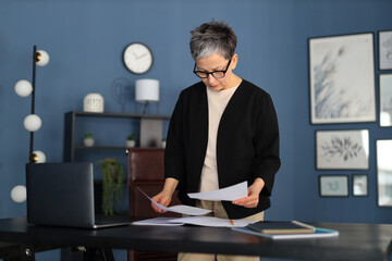 In her workplace, an aged Caucasian businesswoman manages paperwork, embodying professionalism and...