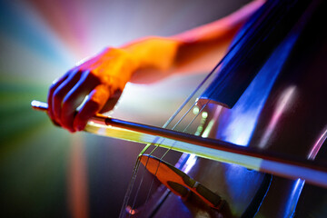 Detailed photo of classical cello with bow in colorful vibrant stage light casting vibrant shadows....