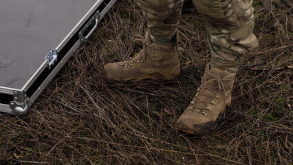 A soldier in uniform stands in a mud near a box with special equipment. close-up of his boots. performing a combat mission in the war. 