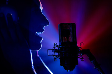 Close-up photo of silhouette of talented singer performing at microphone under vibrant red and blue...