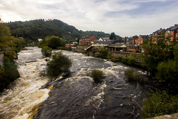 Fototapeta na wymiar View over the rushing water of the River Dee from the Medieval bridge in the Town of Llangollen in Northwest Wales