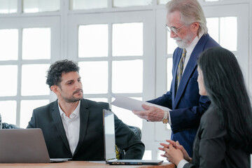 Multigenerational business team engaged in active discussion with a woman taking notes and a man on a call. A collaborative team of professionals in a meeting with one woman writing.