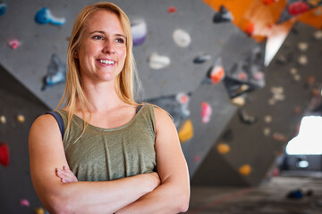 Fototapeta premium Portrait Of Female Coach In Front Of Climbing Wall At Indoor Centre With Climber In Background