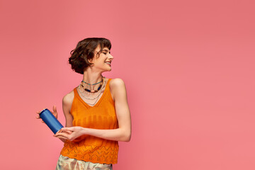 cheerful young woman with short brunette hair and piercing holding soda can on pink, summer drink